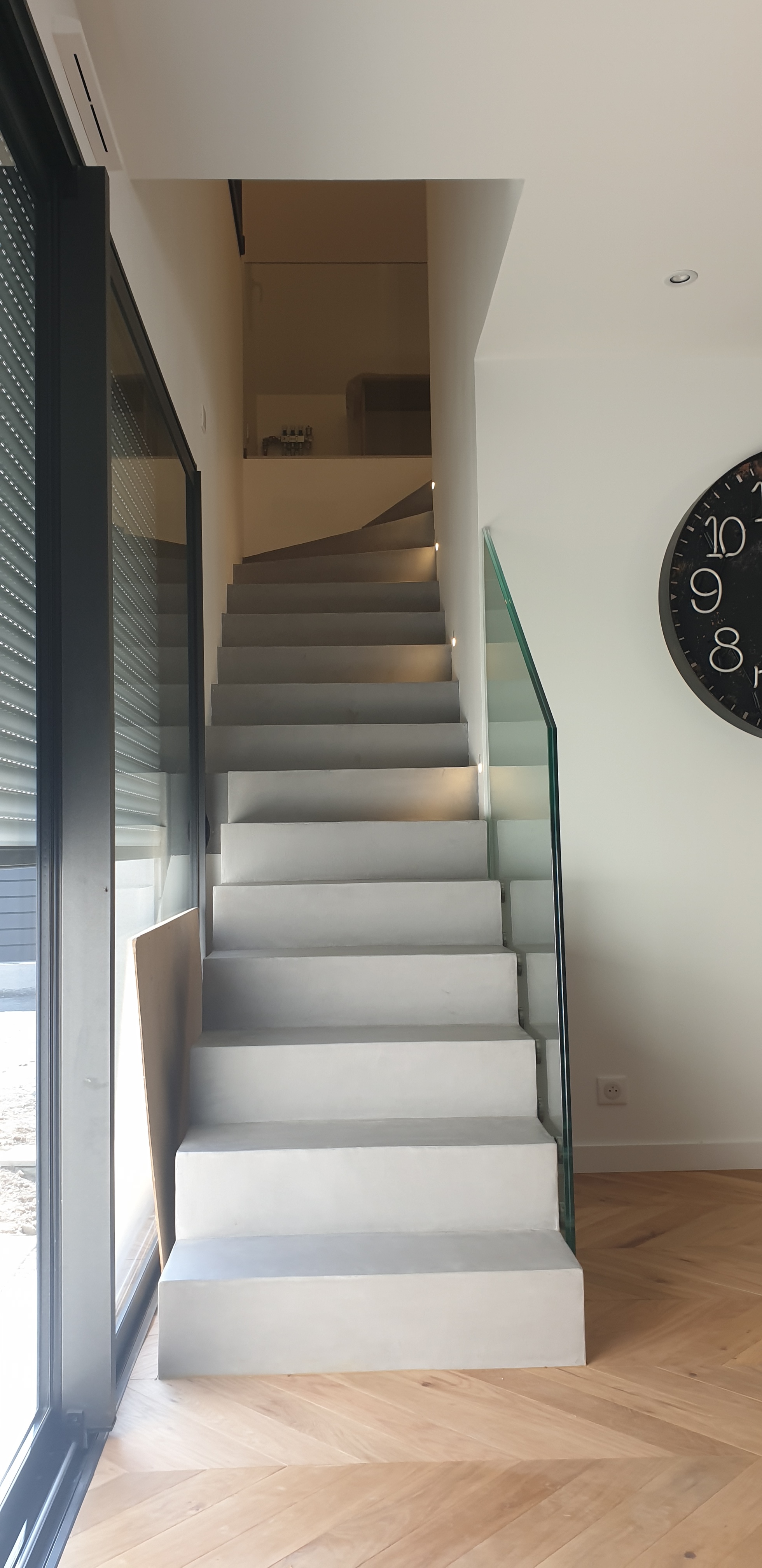 Départ d'un escalier joliment décoré avec un garde corps en verre et un béton ciré