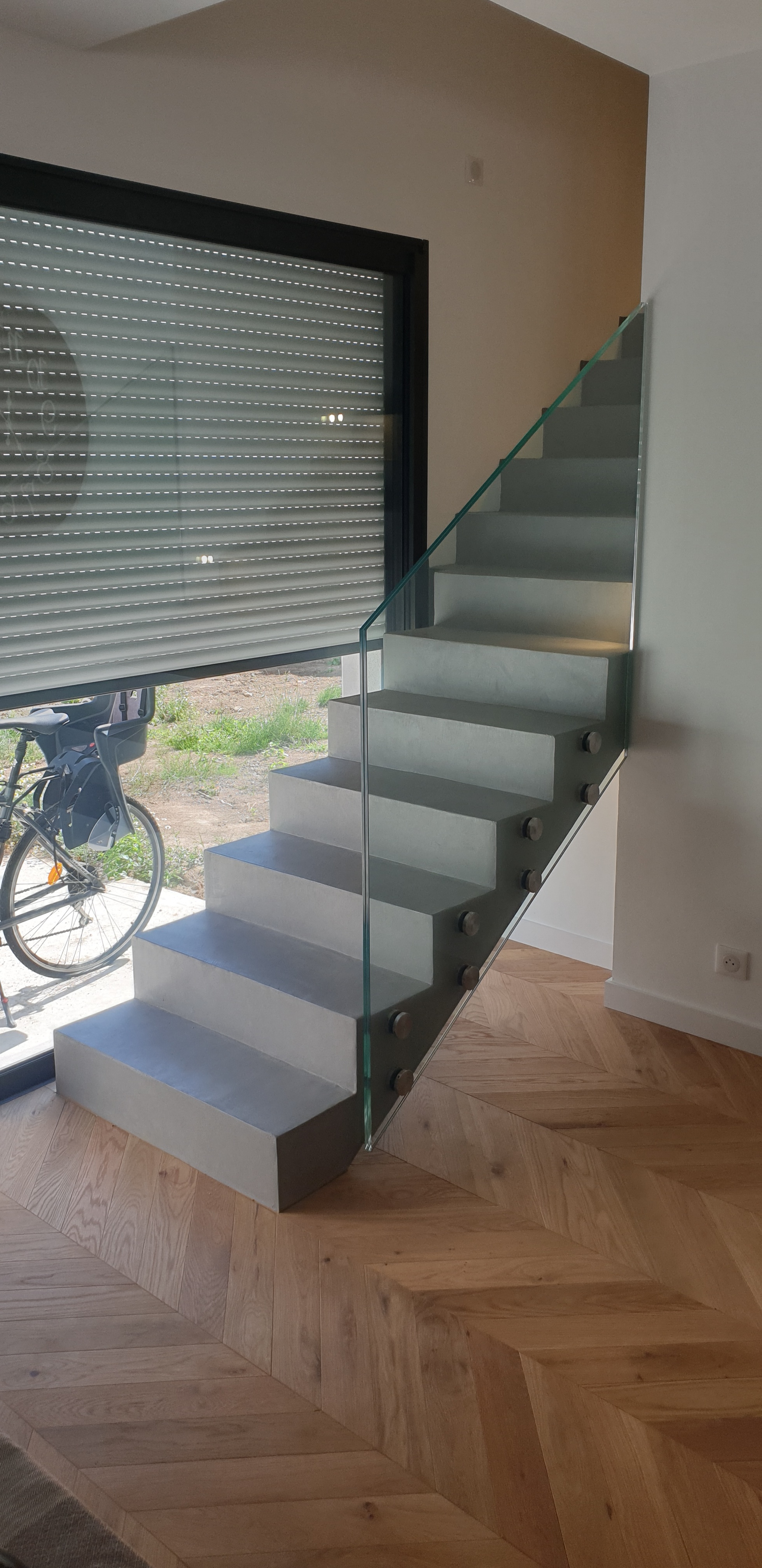 Escalier en béton sur parquet devant une baie vitrée