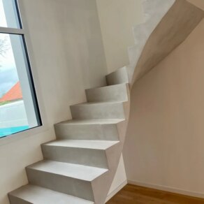 Ce type d'escalier présente une structure en béton ciré moderne et élégante, avec un quart de tour ajoutant une touche de sophistication.